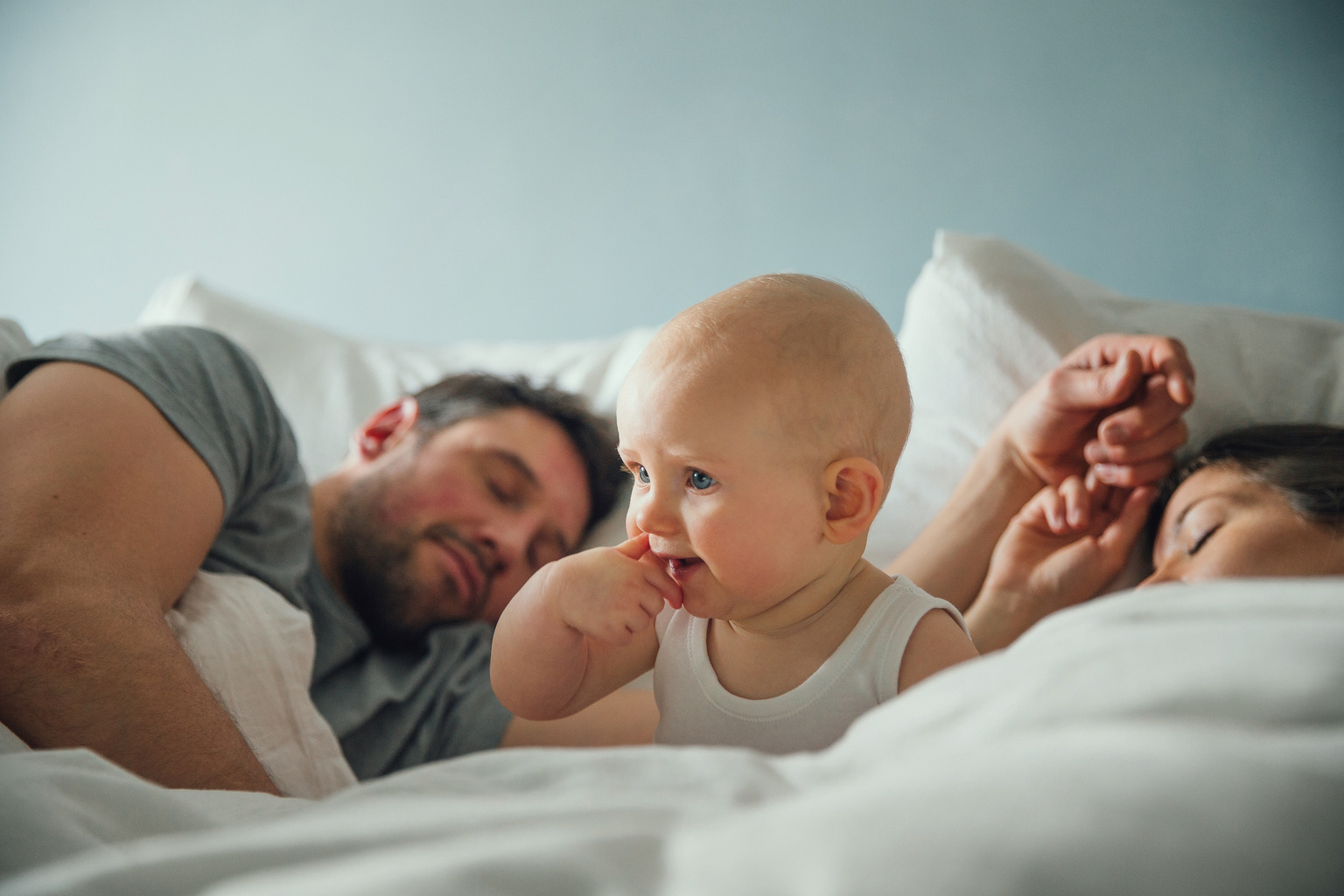 Ein Baby wach im Bett zwischen zwei schlafenden Erwachsenen.